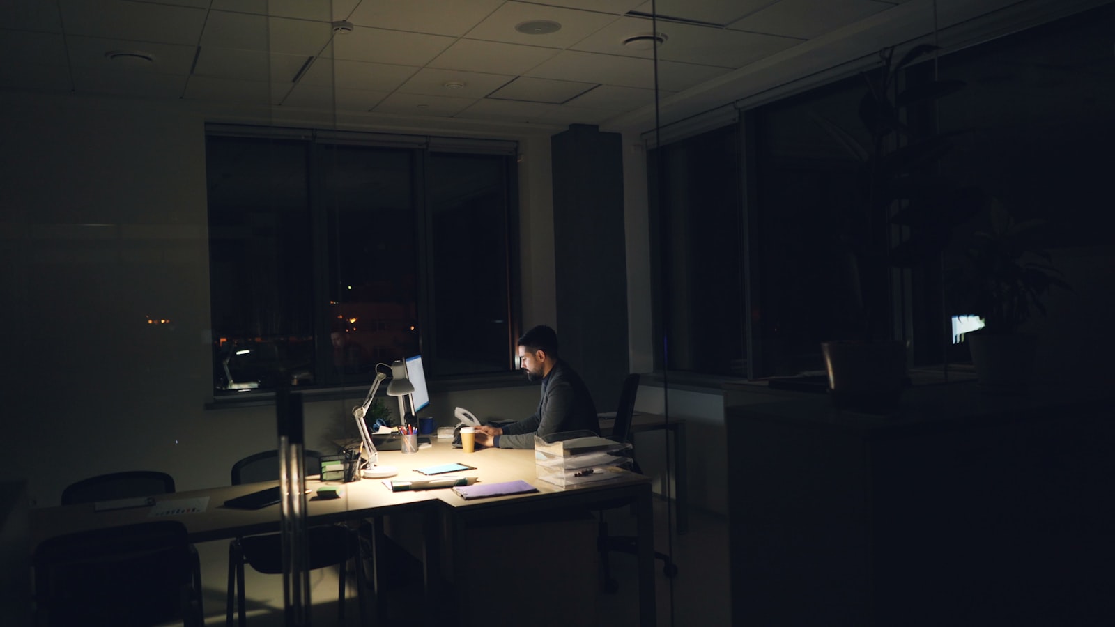 Empresário trabalhando tarde da noite em escritório com luz baixa, sobrecarregado com tarefas operacionais