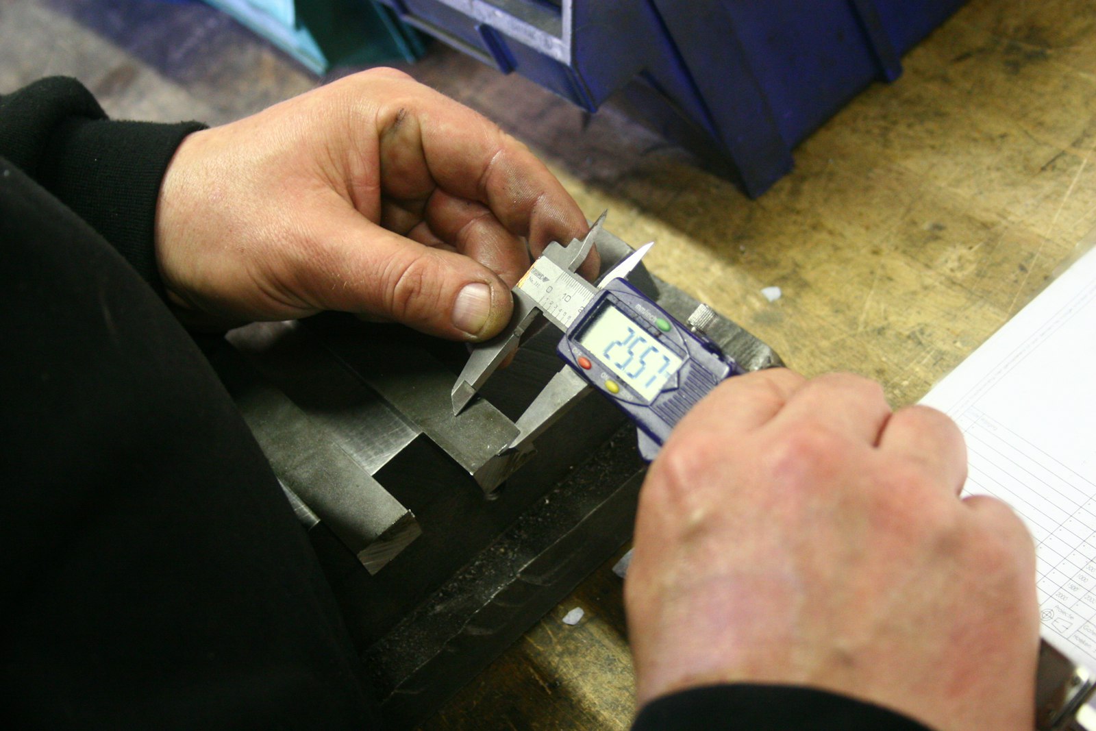 Mãos usando paquímetro digital para medir peça metálica em controle de qualidade industrial