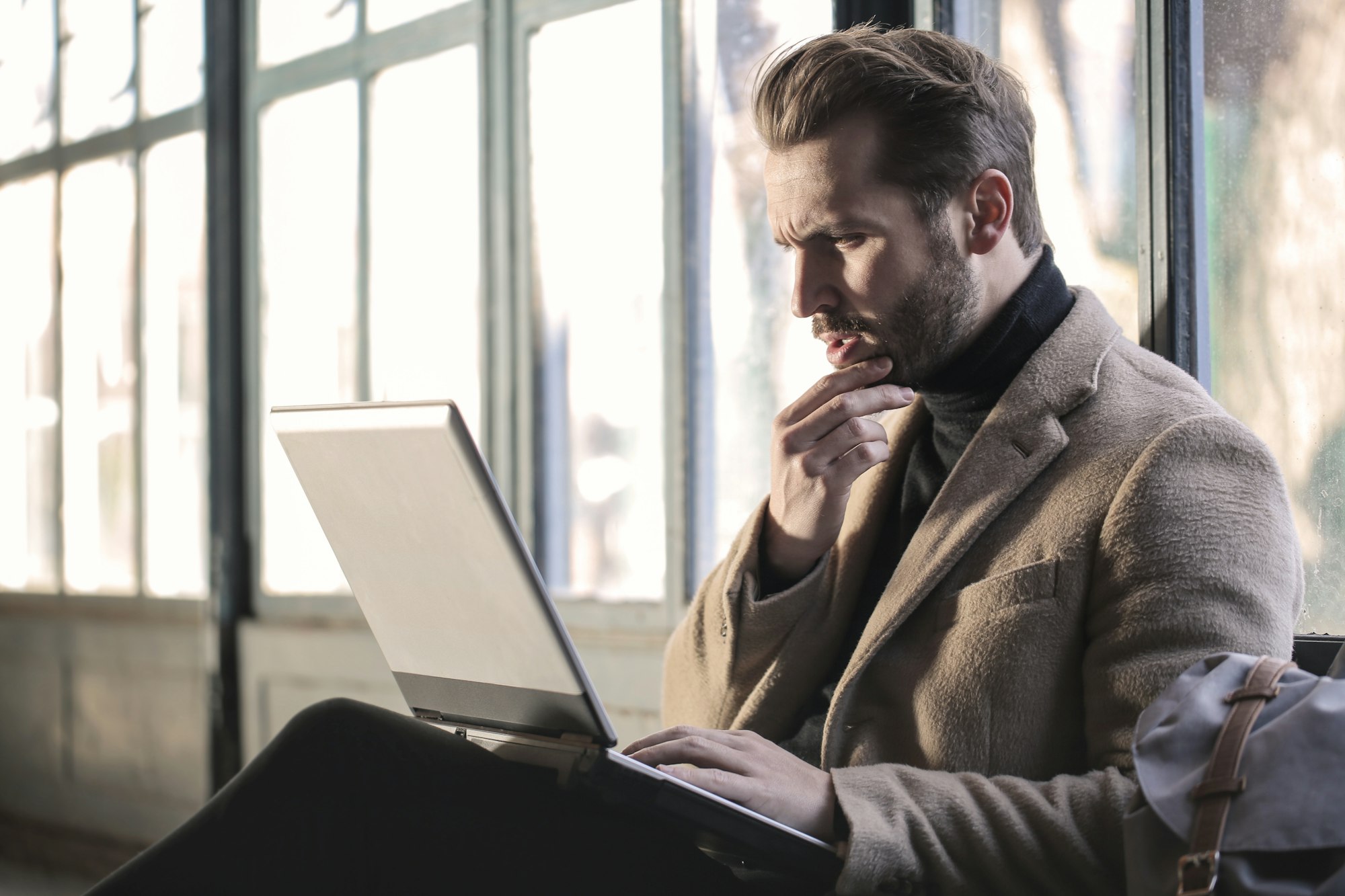 Empresário com a mão no queixo diante do notebook, refletindo sobre uma decisão difícil